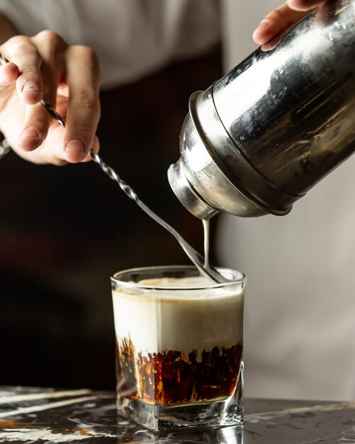 Le barman verse de la crème dans du café glacé à l'aide de la cuillère