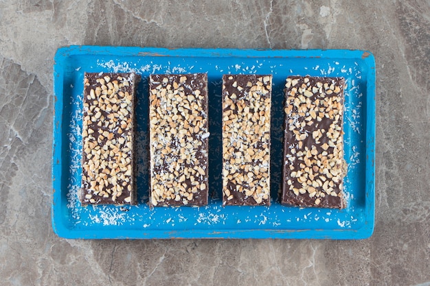 Barre de chocolat en tranches avec noix sur plaque de bois sur marbre.