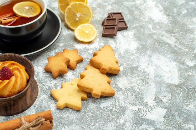 Bas vue rapprochée une tasse de thé tranches de citron bâtons de cannelle biscuits chocolat sur surface grise espace libre