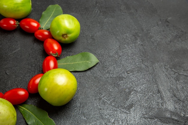 Bas vue rapprochée tomates cerises tomates vertes et feuilles de laurier sur fond sombre