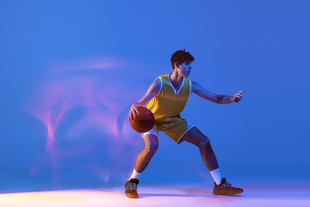 Basket-ball de formation de jeune homme sportif isolé sur dégradé en néon. Ballon dribble