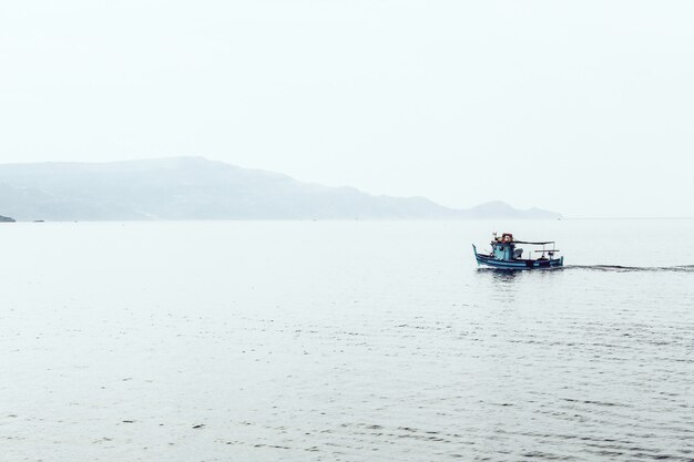 Bateau à moteur sur la mer entouré de montagnes enveloppées de brouillard