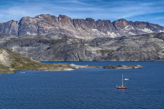 Bateau rouge sur la mer bleue vue montagne grise sous un ciel bleu et blanc