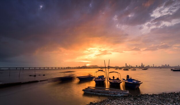 Bateaux à moteur garés sur l'eau au bord de l'eau avec coucher de soleil et une ville visible