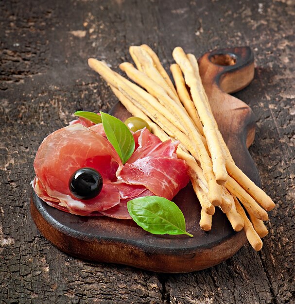 Bâtonnets de pain grissini au jambon, olives, basilic sur vieux bois