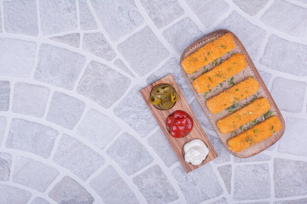 Bâtonnets de pépites de poulet sur un plateau en bois avec des sauces.