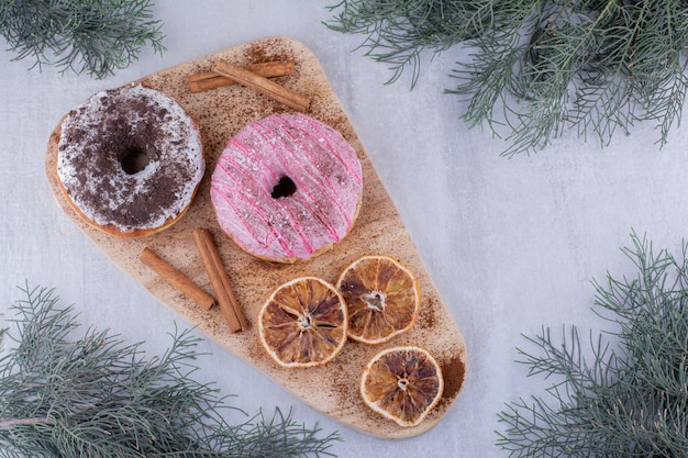 Bâtons de cannelle, beignets et tranches d'orange séchées sur une planche sur fond blanc.