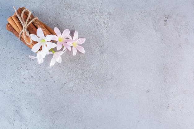 Bâtons de cannelle en corde avec des fleurs blanches et roses sur fond gris.