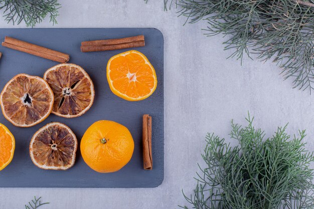 Bâtons de cannelle avec des oranges juteuses et des tranches séchées sur une planche à découper sur fond blanc. Photo de haute qualité