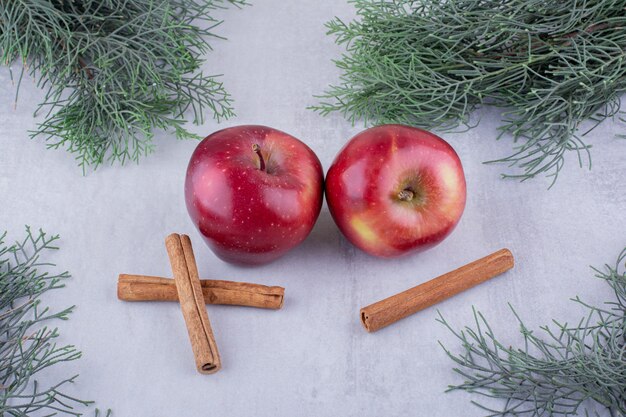 Les bâtons de cannelle et les pommes se regroupent entre les branches de pin sur fond blanc.