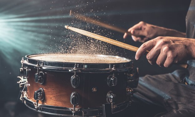 Le batteur à l'aide de baguettes frappant la caisse claire avec des éclaboussures d'eau sur fond noir sous l'éclairage de studio se bouchent.