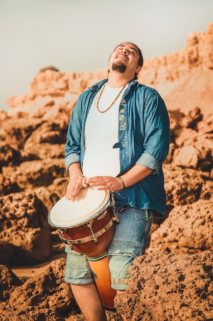 Photo gratuite batteur de boho jouant au tambour sur la plage sur les pierres