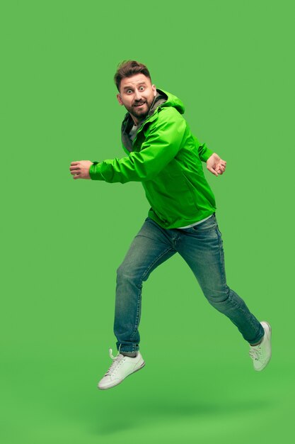 Beau barbu souriant heureux jeune homme en cours d'exécution isolé sur un studio vert branché vif. concept de l'automne et du temps froid. Concepts d'émotions humaines