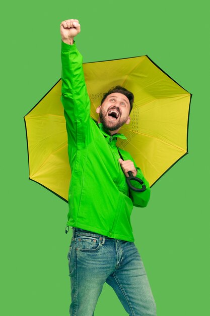 Beau barbu souriant heureux jeune homme tenant un parapluie et regardant la caméra isolée sur un studio vert branché vif.