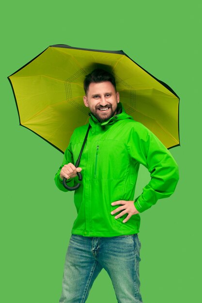 Photo gratuite beau barbu souriant heureux jeune homme tenant un parapluie et regardant devant isolé sur un studio vert branché vif