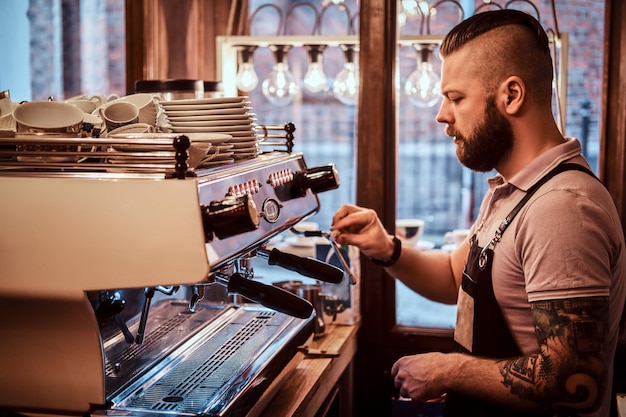 Beau barista en uniforme faisant du café pour un client dans le café