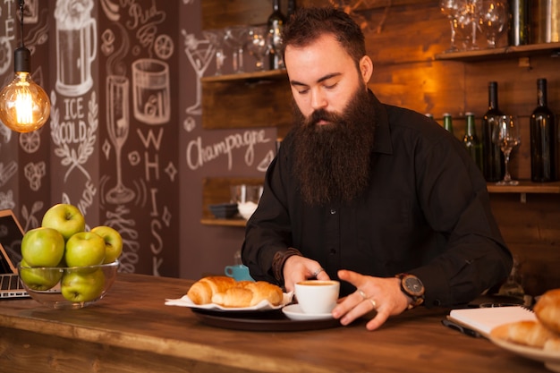 Beau barman derrière un bar avec un café préparé. Pub vintage.