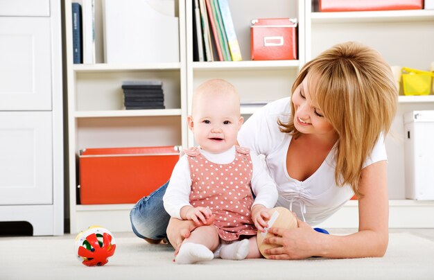 Beau bébé jouant avec des jouets avec une mère heureuse à l'intérieur