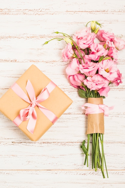 Photo gratuite beau bouquet de fleurs fraîches d'eustoma rose avec une boîte présente sur une surface en bois