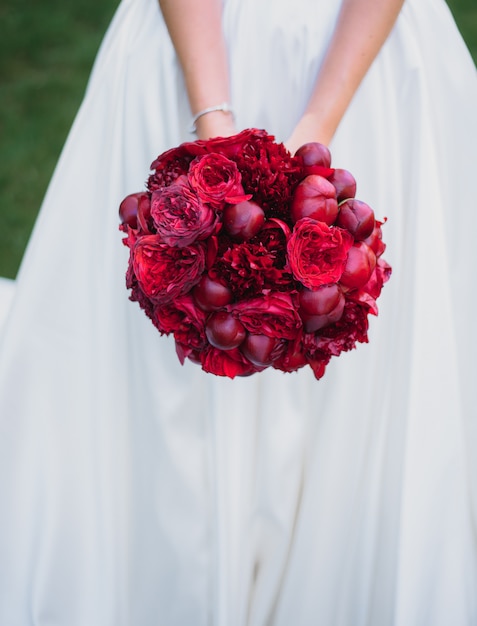 Beau bouquet de mariée rouge fait de pivoines dans les mains de la mariée