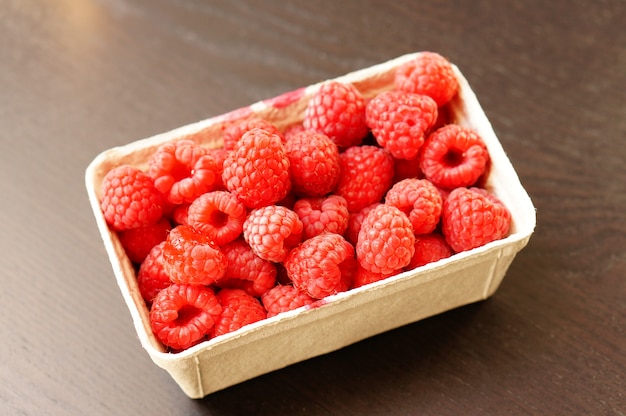 Beau coup de framboises fraîches dans une assiette en plastique sur la table en bois