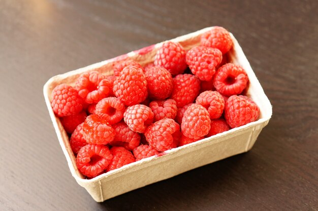 Beau coup de framboises fraîches dans une assiette en plastique sur la table en bois