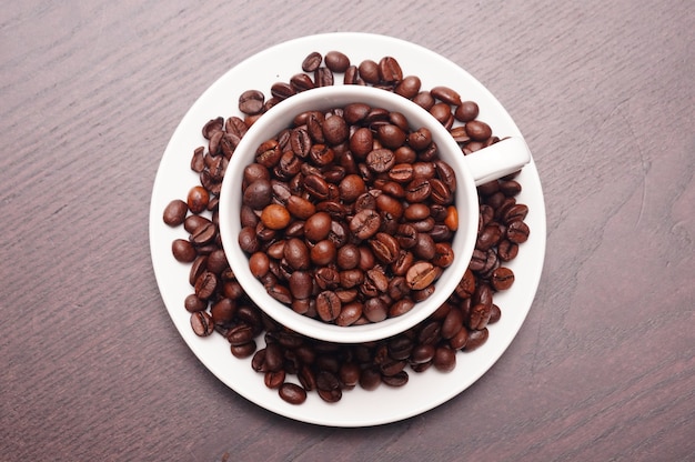 Beau coup de grains de café dans la tasse blanche et plaque sur une table en bois