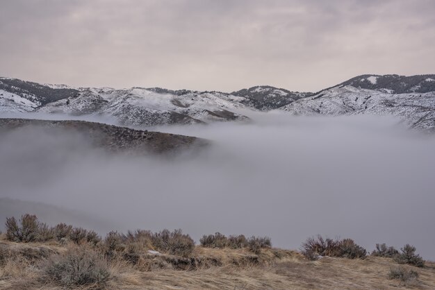 Beau coup de montagnes enneigées au-dessus du brouillard avec un ciel nuageux