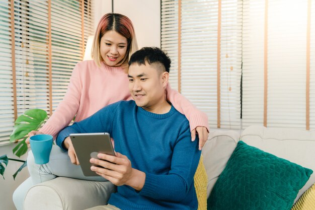 Beau couple asiatique attrayant avec tablette en position allongée sur le canapé pour se détendre dans leur salon