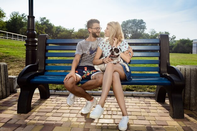 Beau couple assis avec bouledogue français sur un banc dans le parc