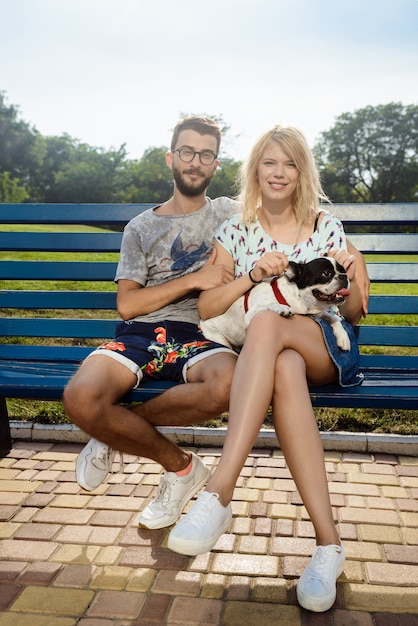 Beau couple assis avec bouledogue français sur un banc dans le parc