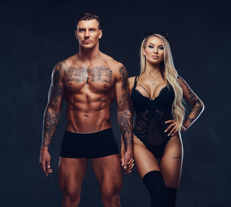 Photo gratuit beau couple, beau mâle tatoué et séduisante fille en sous-vêtements noirs tenant par la main, posant en studio.