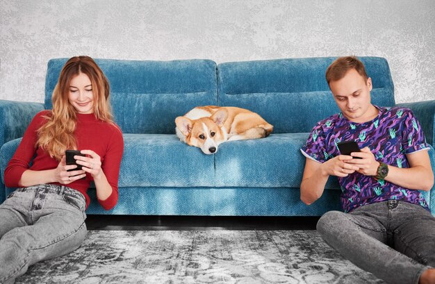 Beau couple avec téléphones portables et mignon Corgi sur canapé