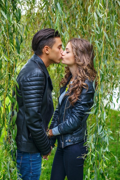 Beau couple en vestes de cuir s'embrasser sous l'arbre vert.