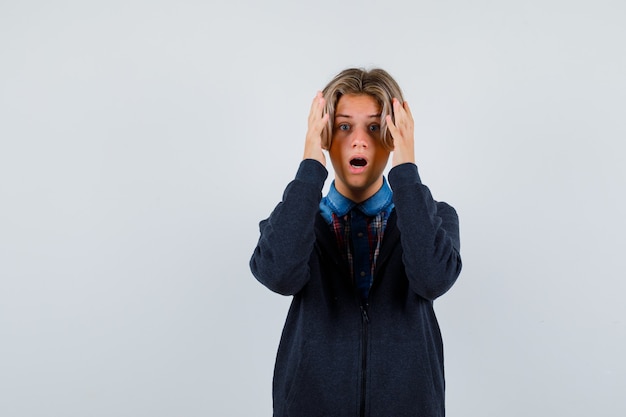 Beau garçon adolescent avec les mains près de la tête en chemise, sweat à capuche et l'air agité. vue de face.