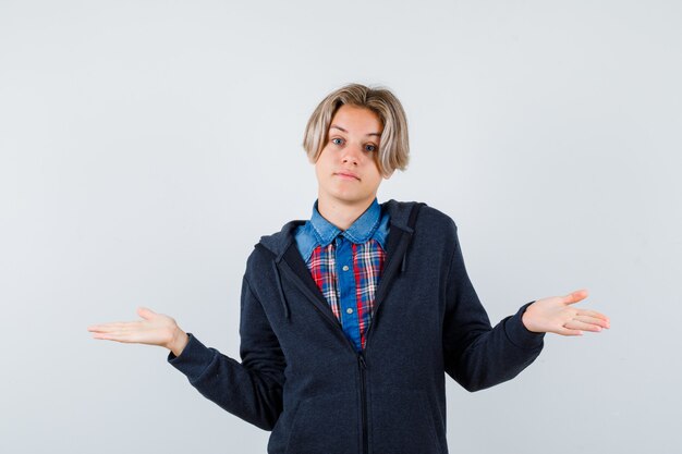 Beau garçon adolescent montrant un geste impuissant en chemise, sweat à capuche et semblant confus. vue de face.