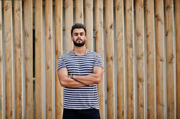 Beau grand modèle homme barbe arabe à chemise dépouillée posé en plein air sur fond de bois