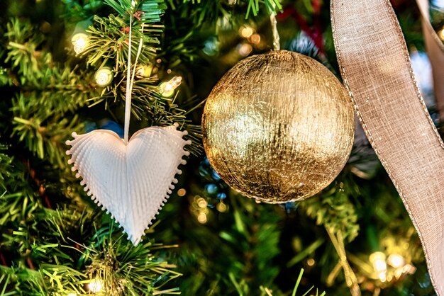 Beau gros plan d'un ornement en forme de coeur blanc et boule d'or sur un arbre de Noël
