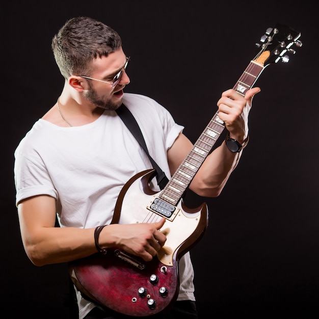 Beau guitariste jouant de sa guitare électrique sur un mur noir