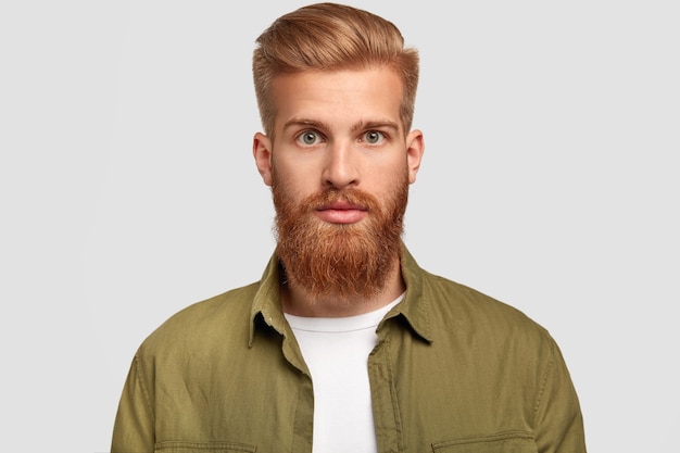 Photo gratuite beau hipster a une barbe de gingembre, une coiffure à la mode, regarde sérieusement directement la caméra, contemple son futur emploi