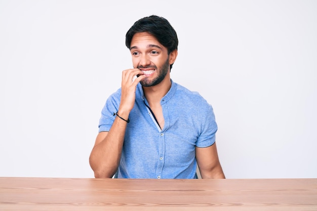 Photo gratuite beau homme hispanique portant des vêtements décontractés assis sur la table et ayant l'air stressé et nerveux avec les mains sur la bouche mordant les ongles problème d'anxiété