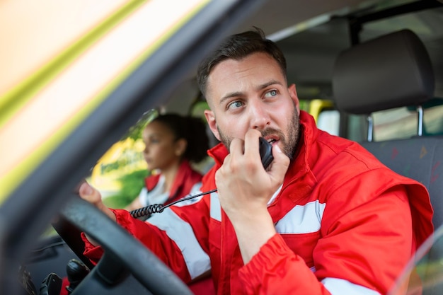 Beau Jeune Ambulancier Paramédical Parlant Par Radio Portable Alors Qu'il était Assis Dans Une Ambulance