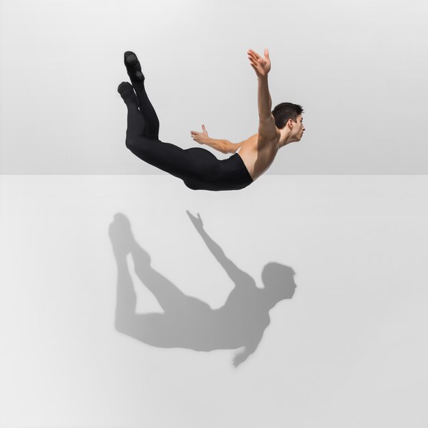 Beau jeune athlète masculin pratiquant sur blanc avec des ombres en saut, vol aérien