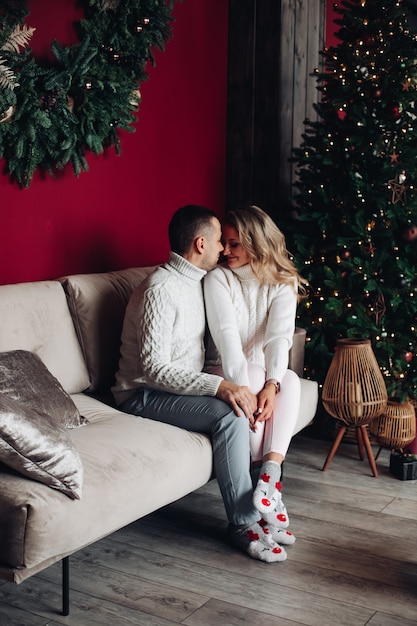 Beau jeune couple d'amoureux s'embrasse sur le canapé à la maison dans l'atmosphère de Noël