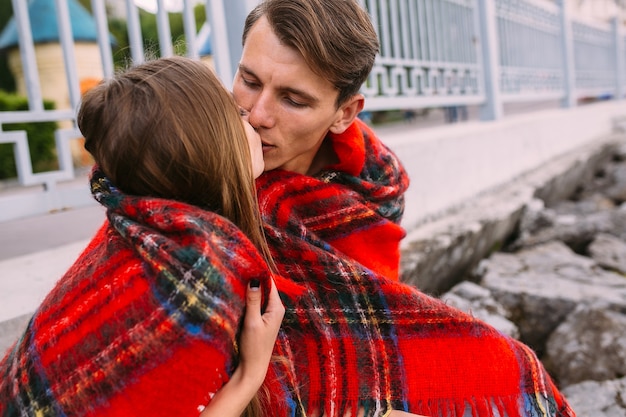 Beau jeune couple assis sur un remblai de pierre, enveloppé dans une couverture