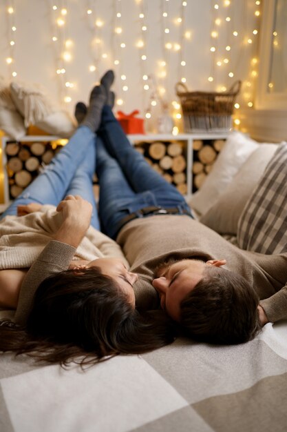 Beau jeune couple heureux se détendre dans son lit et souriant, embrassant