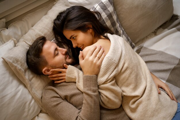 Beau jeune couple heureux se détendre dans son lit et souriant, embrassant