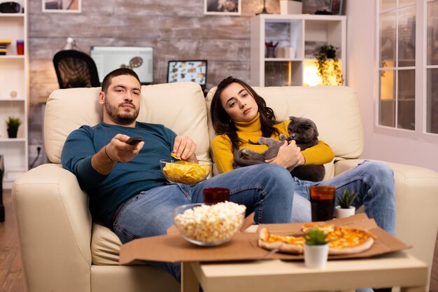 Beau jeune couple regardant la télévision et mangeant des plats à emporter dans le salon