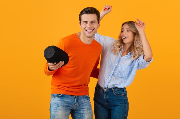 Beau jeune couple souriant tenant un haut-parleur sans fil écoutant de la musique dansant une humeur heureuse de style coloré émotionnel isolé sur fond jaune