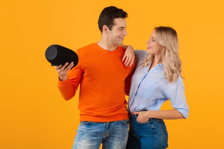 Photo gratuit beau jeune couple souriant tenant un haut-parleur sans fil écoutant de la musique